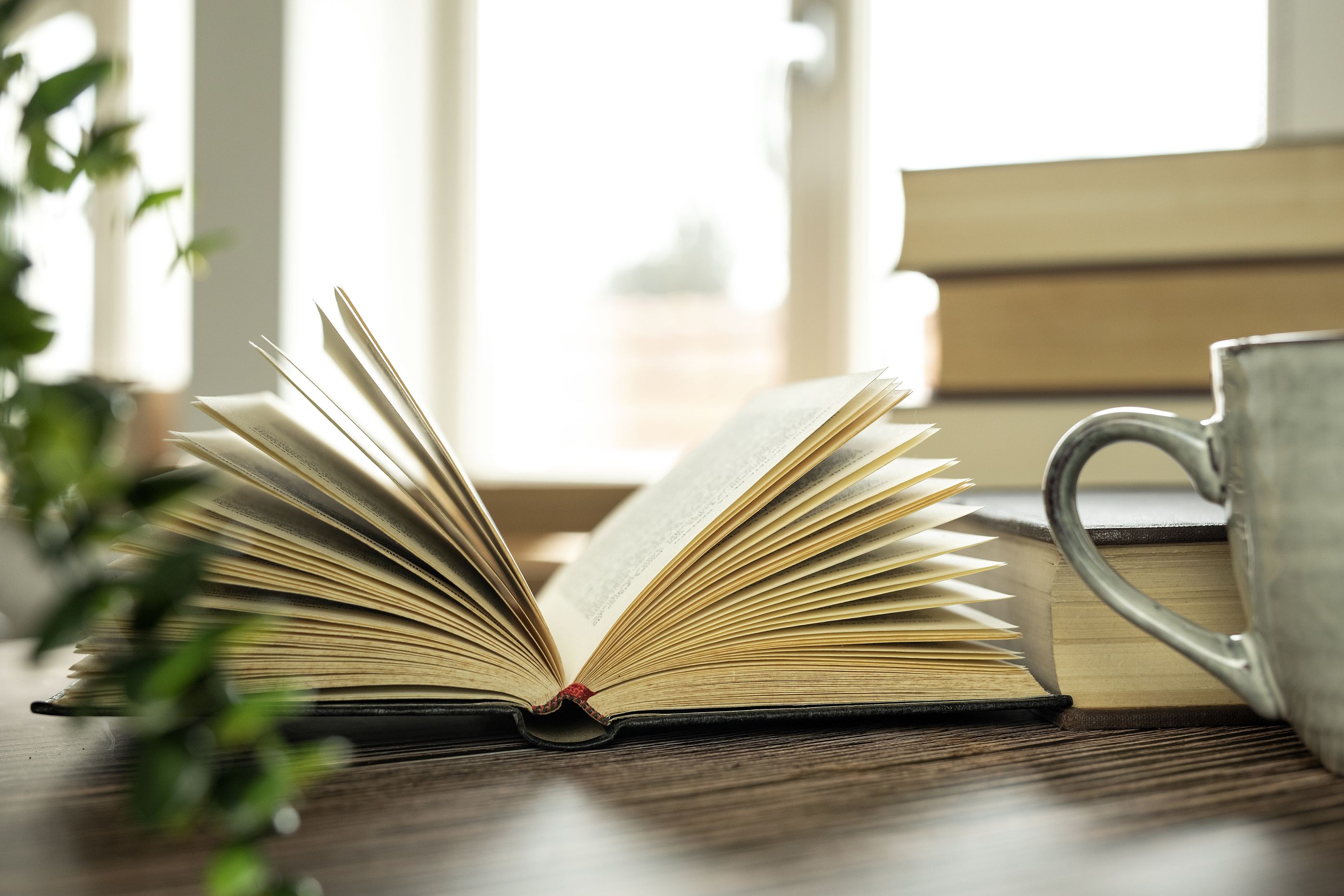 Öppen bok och kaffekopp, flera böcker i bakgrunden.