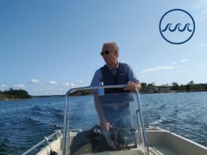 Erik Bonsdorff kör en båt. I bakgrunden synd blått hav och blå himmel.