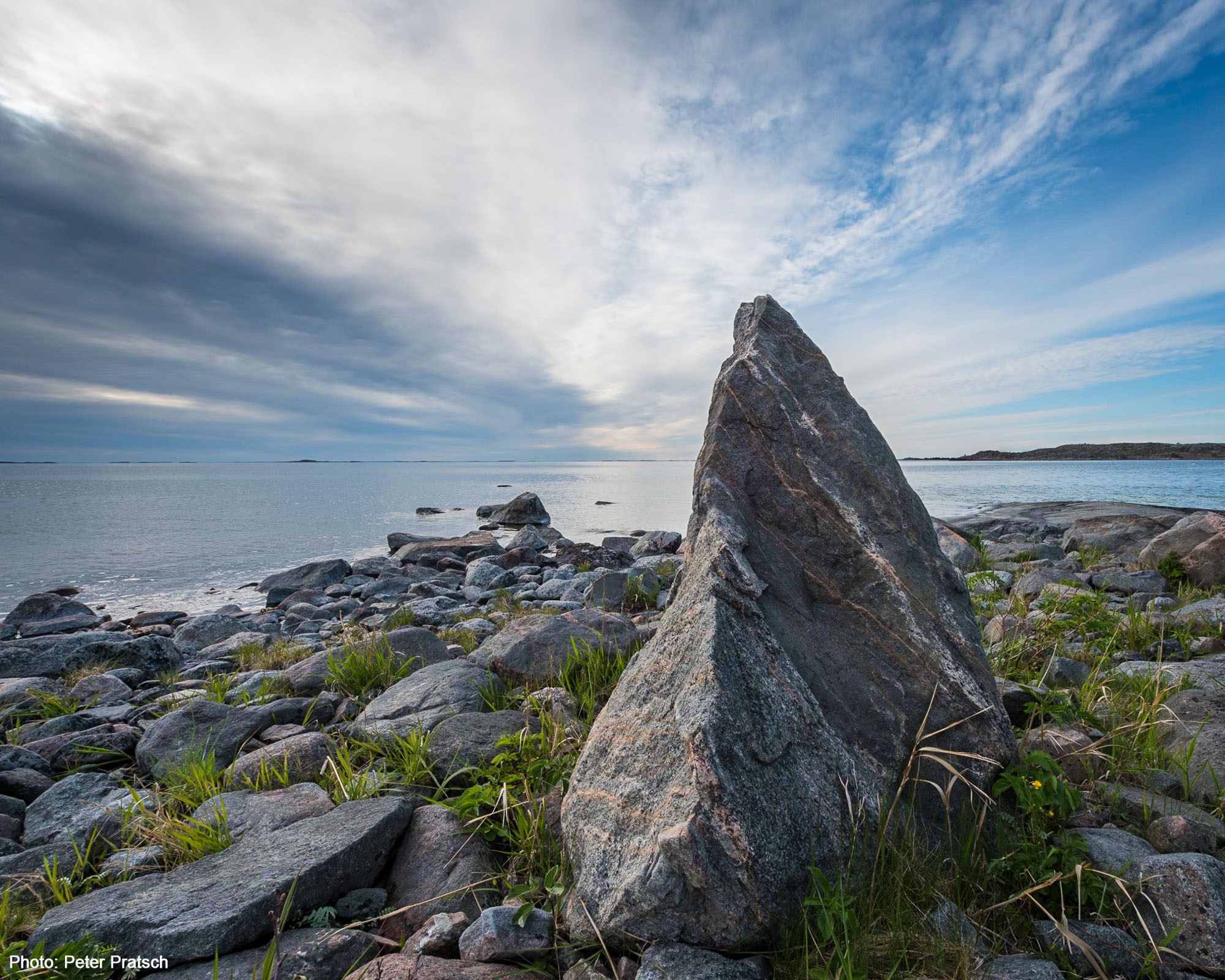 Kustremsa med en större uppåt pekande sten centralt i bilden