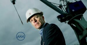 Kim Wikström står framför en lyftkran. Bakgrunden är hotfullt grå. I det nedre vänstra hörnet syns en logo bestående av tre vågor inne i en cirkel.