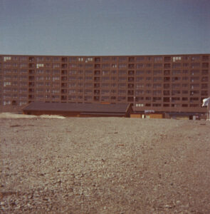 Bostadsområde på 1970-talet i Sverige, rödbrunt höghus med stort grusfält i förgrunden.